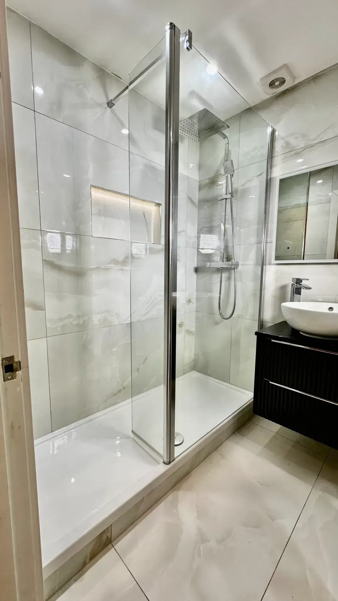 A bathroom with a walk in shower , sink and mirror.