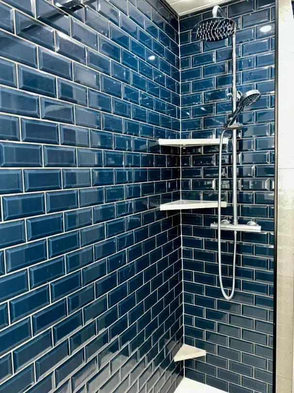 A shower with blue subway tiles and a shower head.