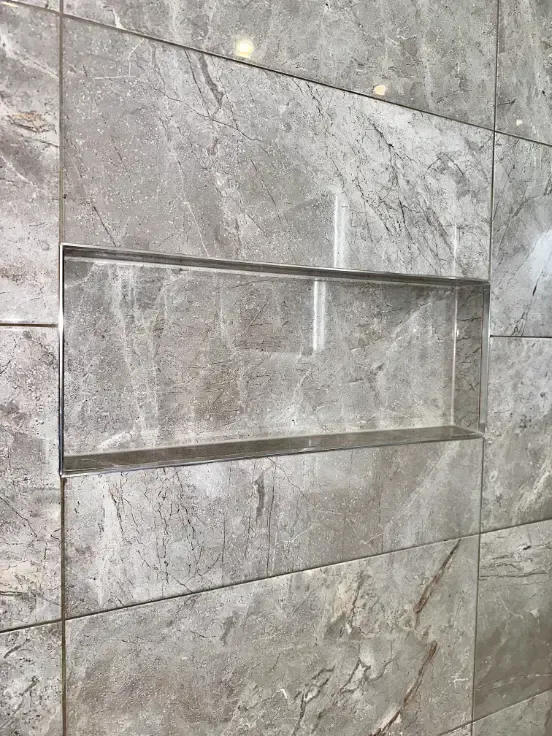 A shower niche in a tiled wall with a stainless steel frame.