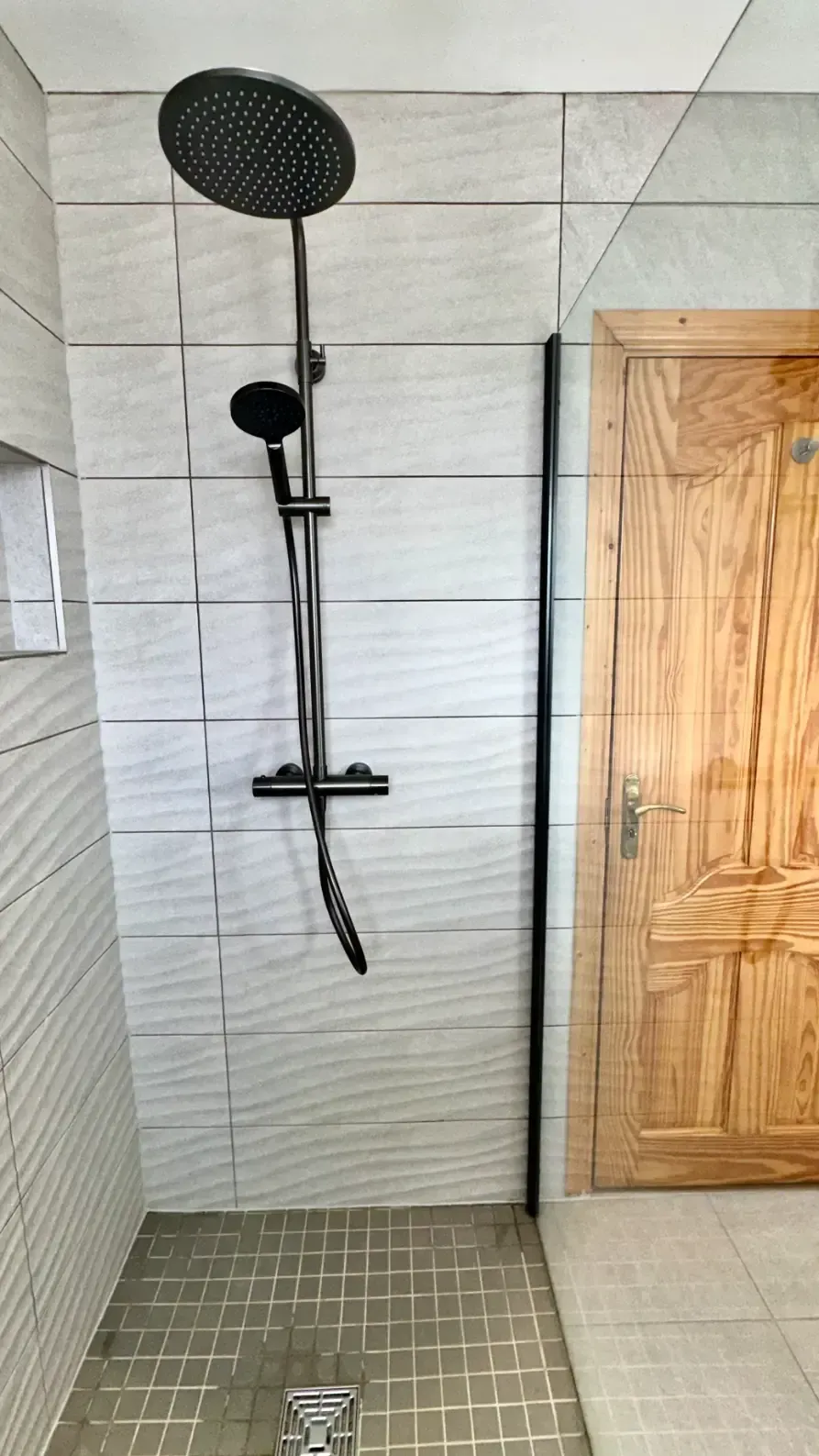 A shower with a black shower head and a wooden door.
