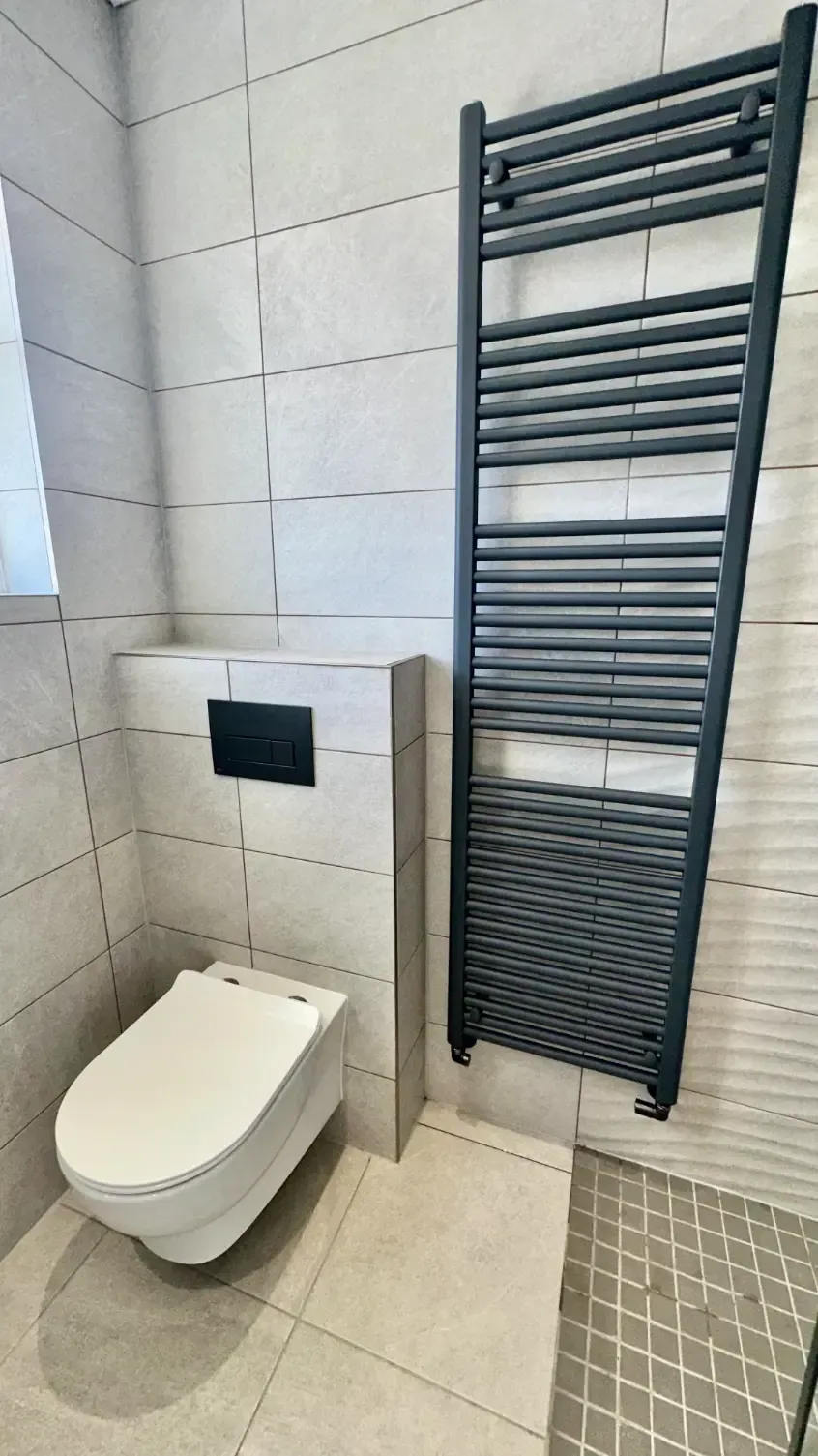 A bathroom with a toilet , towel rack and shower.