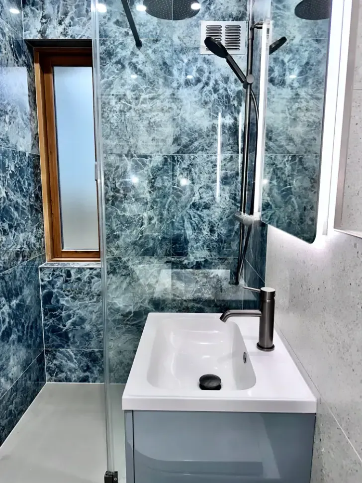 A bathroom with a sink , shower , mirror and window.