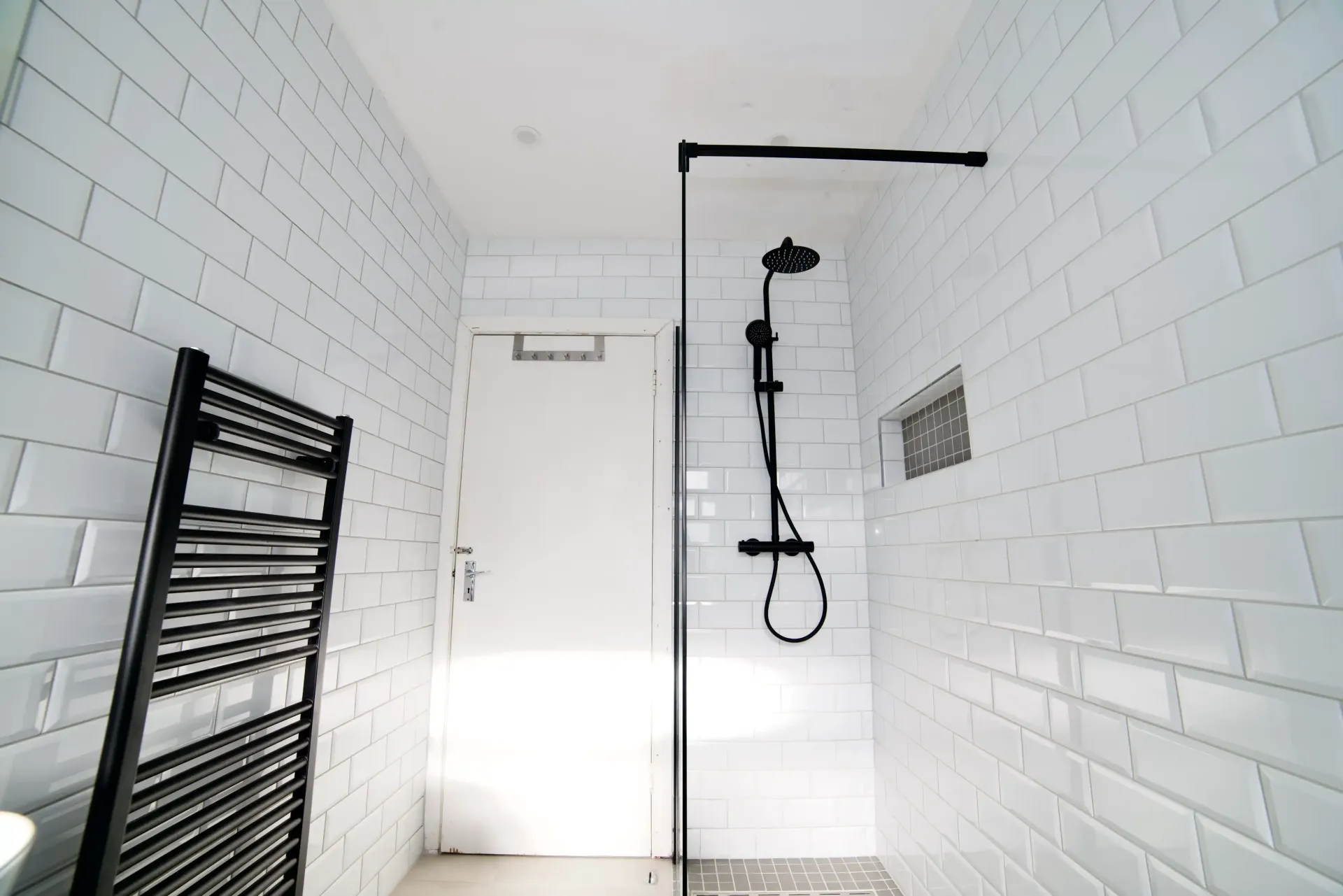 A bathroom with white tiles and a black towel rack.
