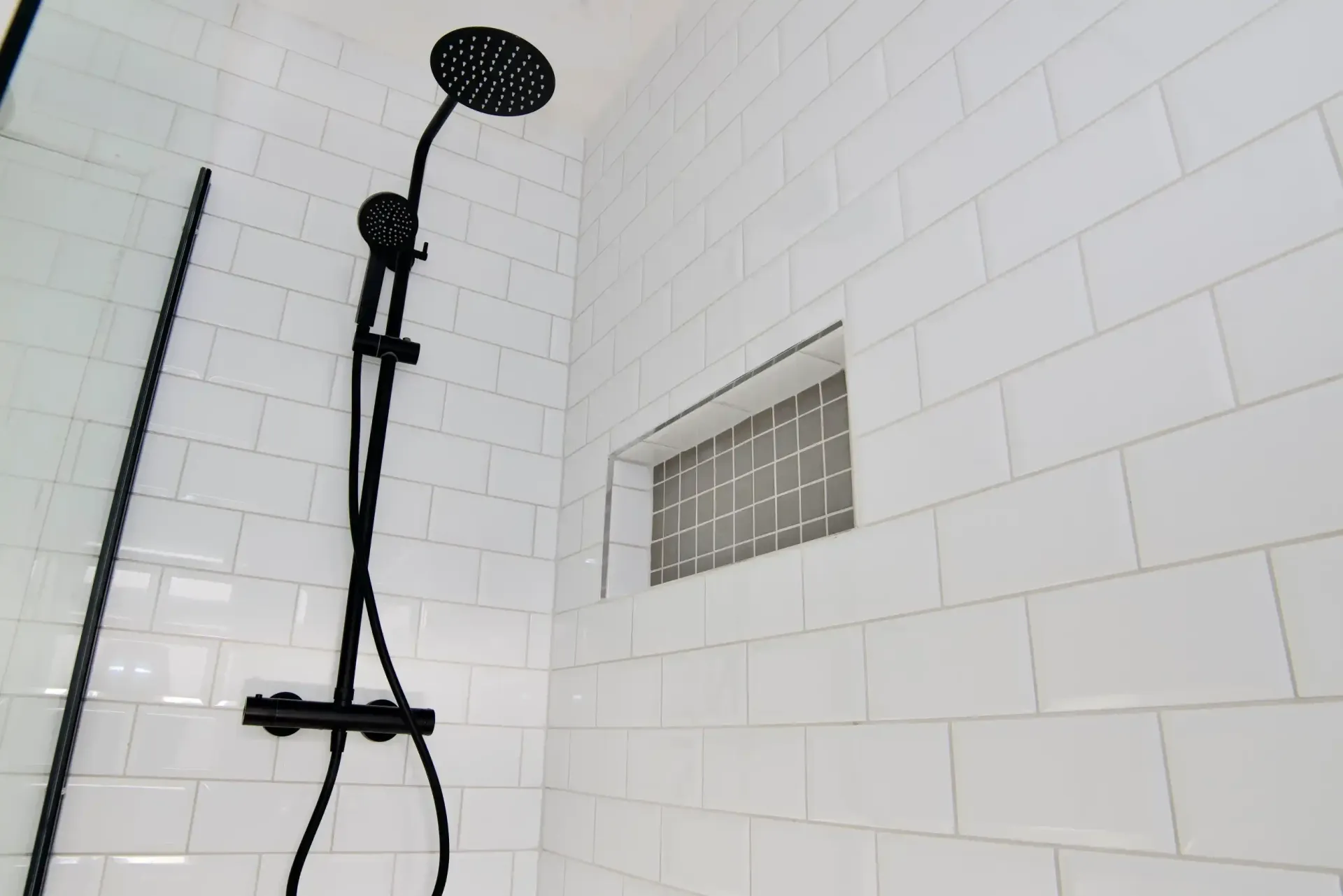 A shower with white tiles and a black shower head.