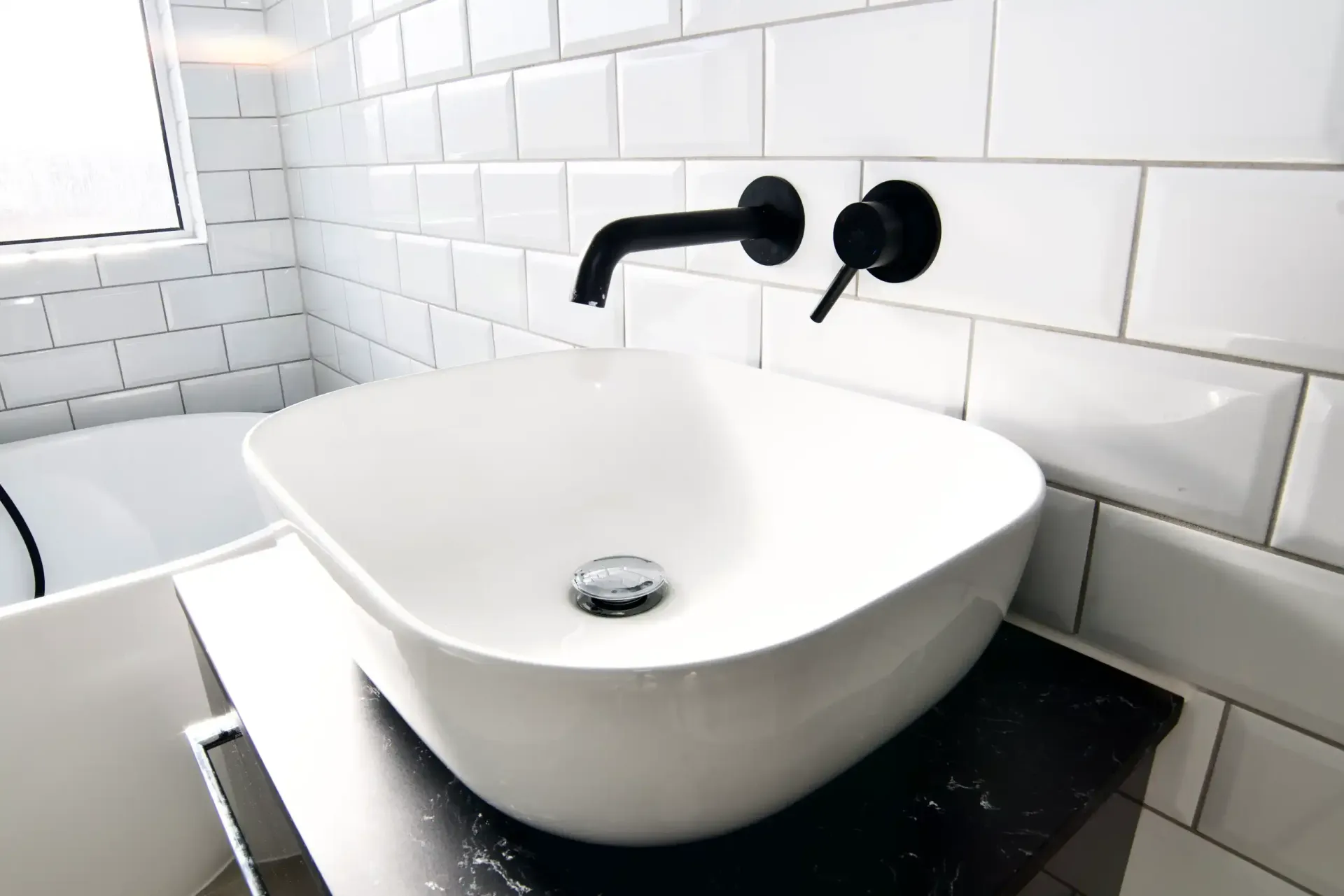 A bathroom sink with black faucets and white tiles