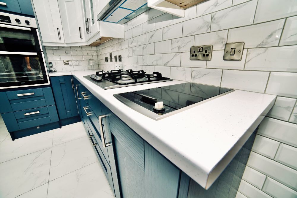 A kitchen with blue cabinets and white counter tops has a stove top oven.