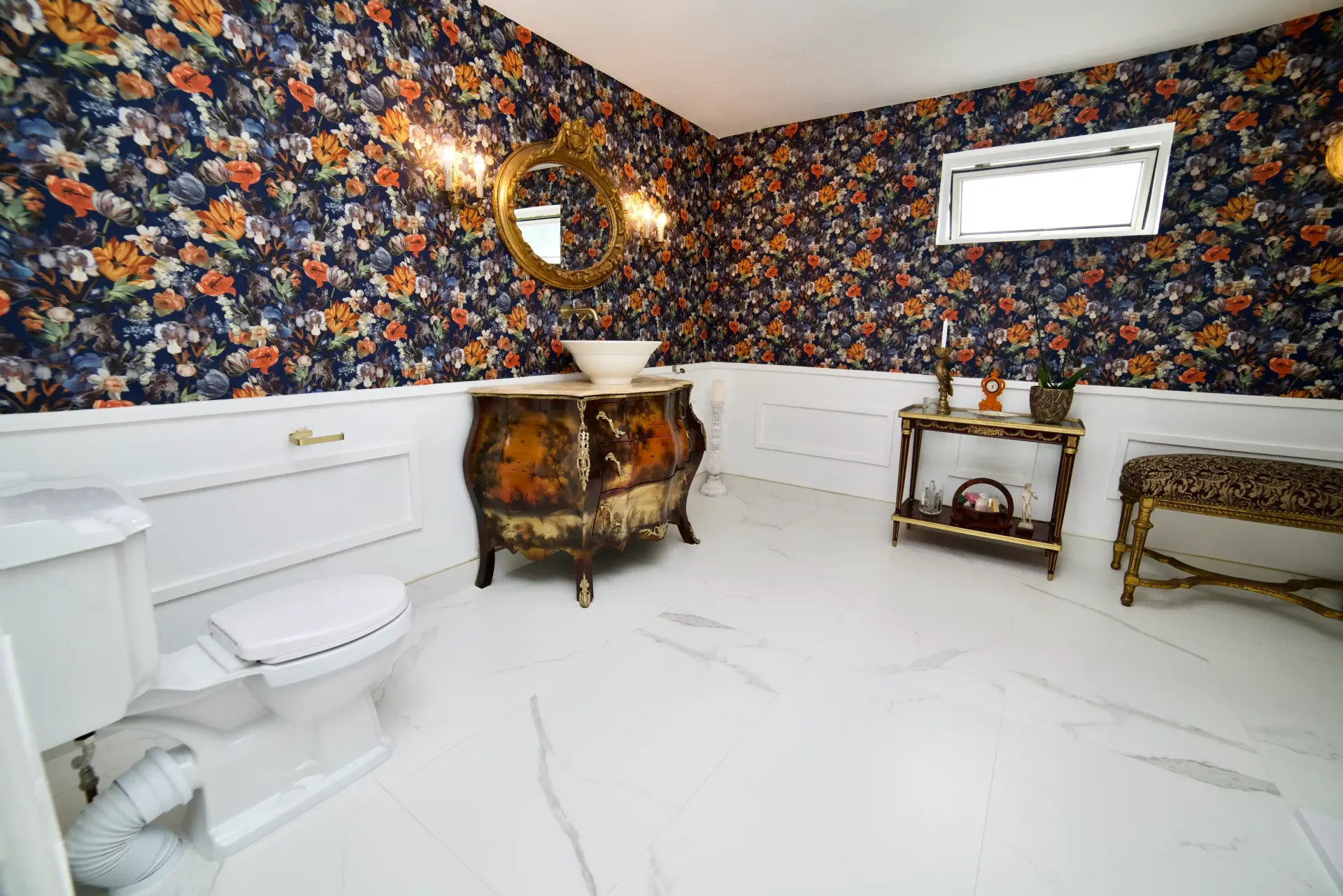 A bathroom with a toilet , sink , mirror and floral wallpaper.