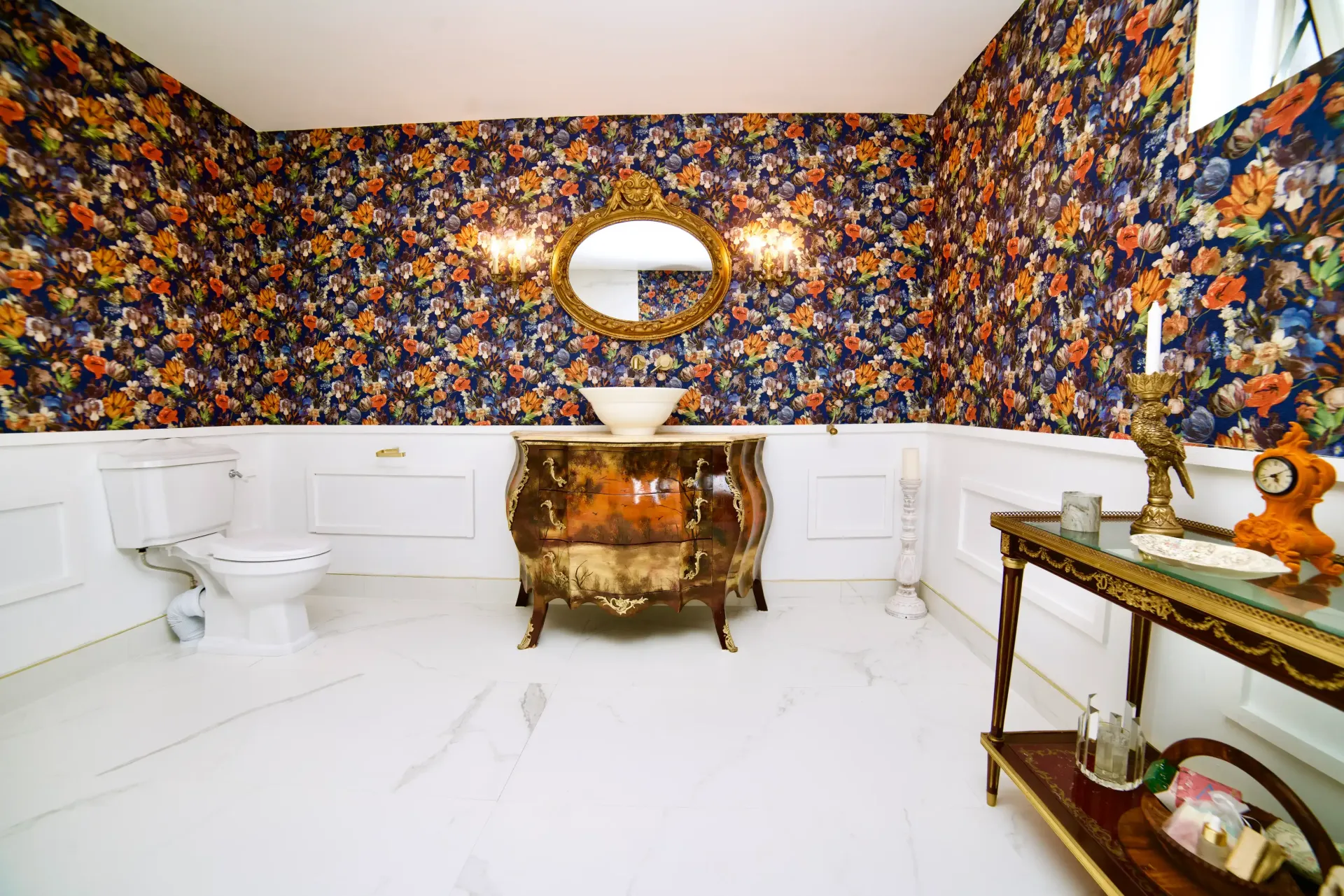 A bathroom with a toilet , sink , mirror and floral wallpaper.
