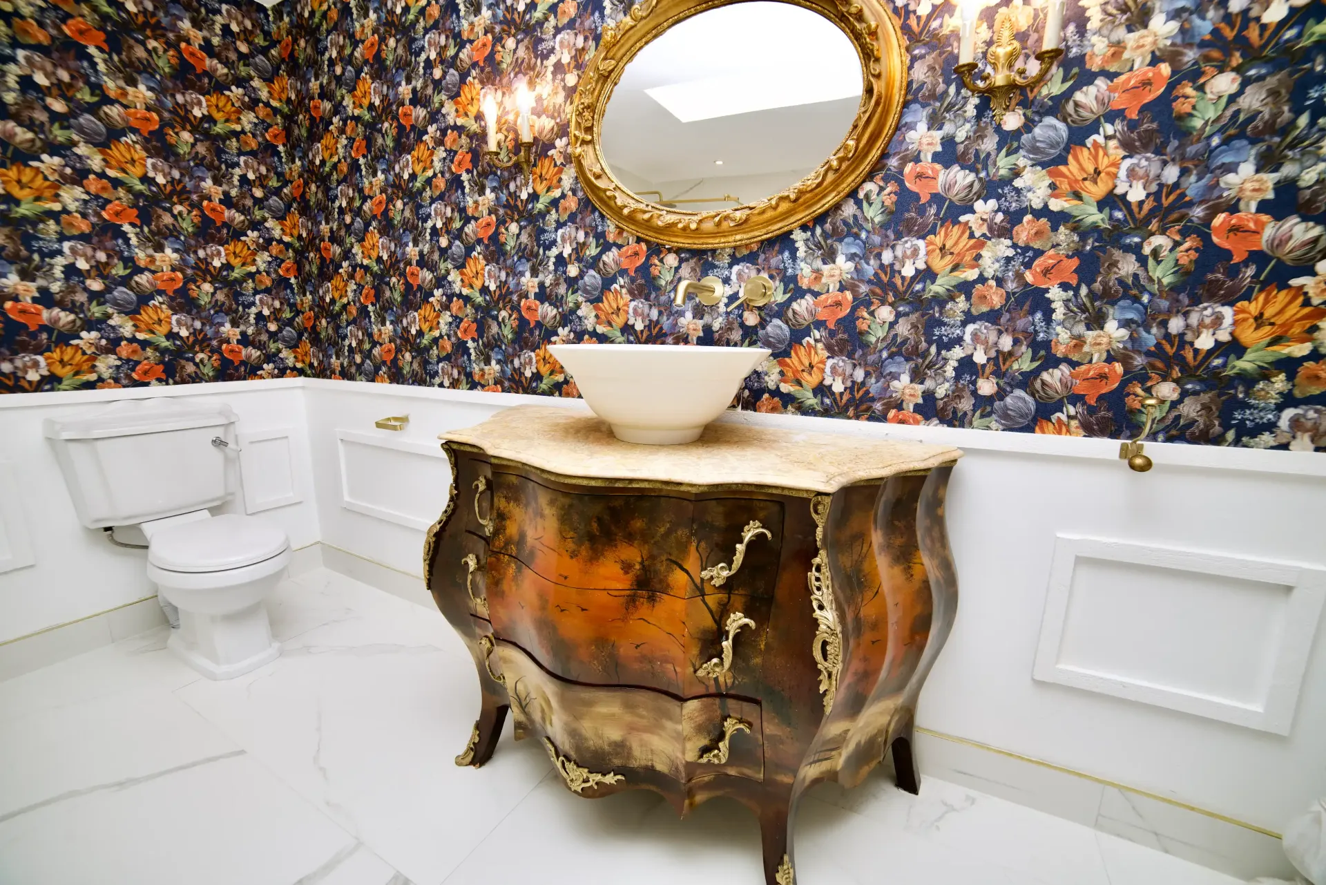 A bathroom with a toilet , sink , mirror and floral wallpaper.