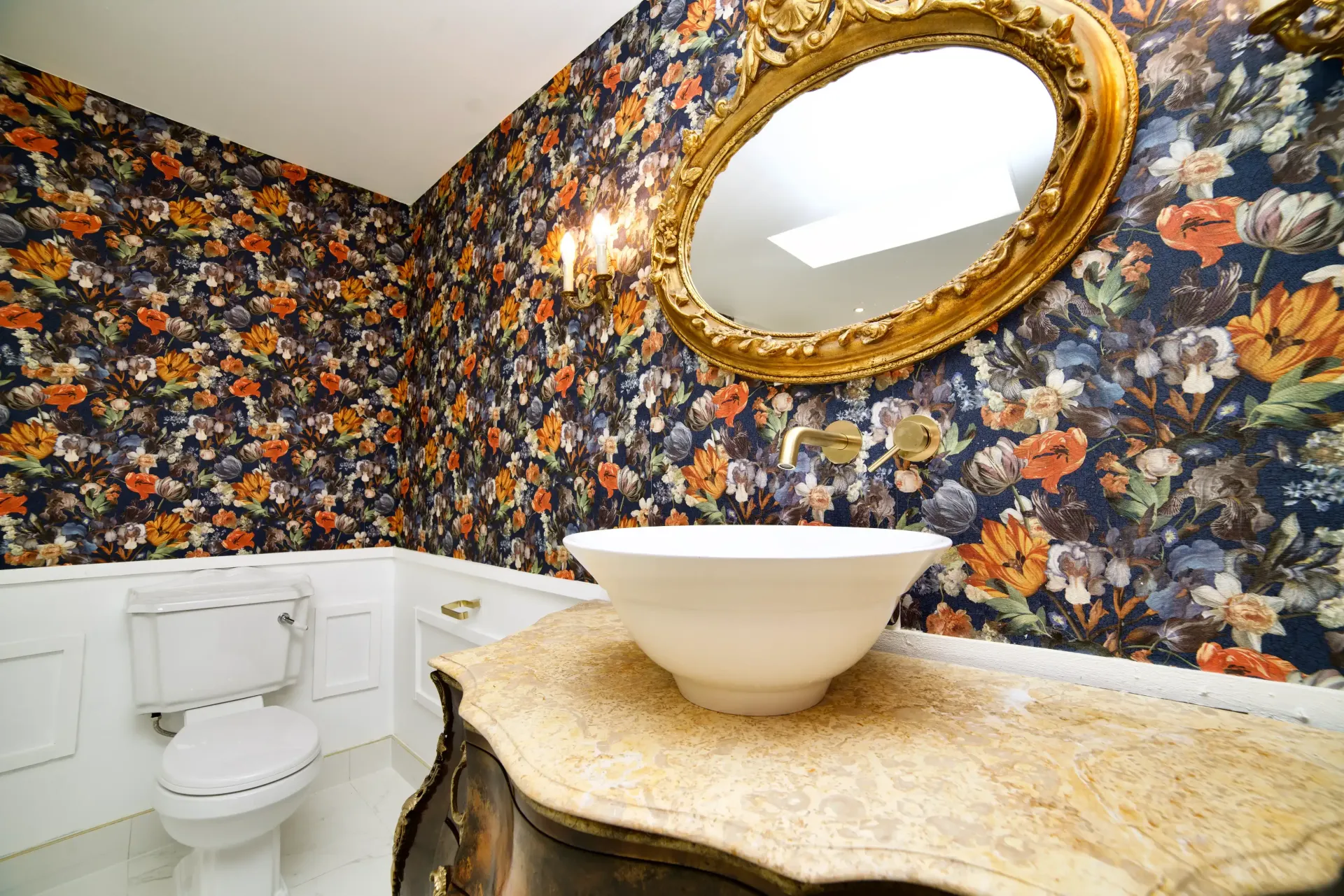A bathroom with a toilet , sink , mirror and floral wallpaper.