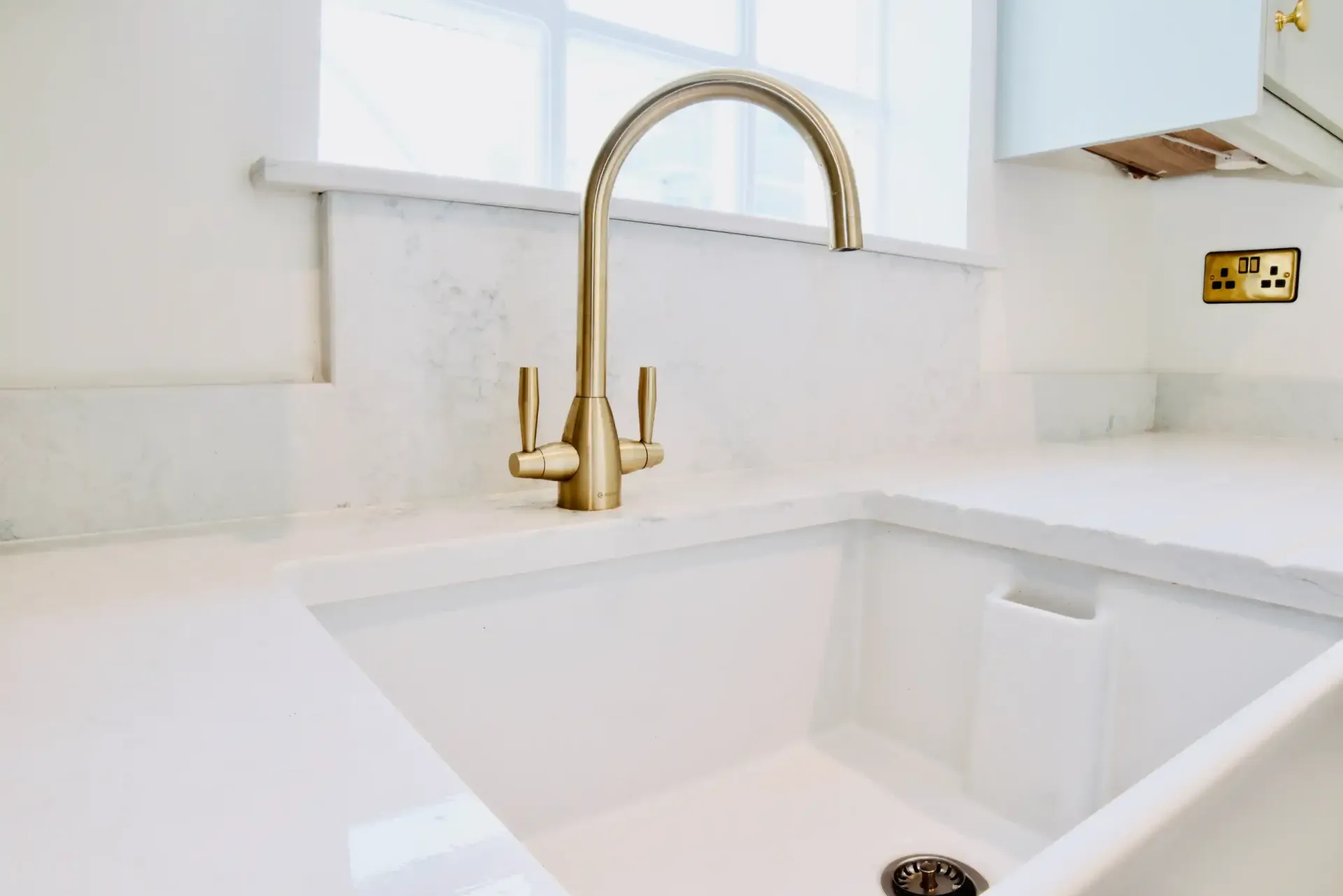 A kitchen sink with a gold faucet and a white counter top.