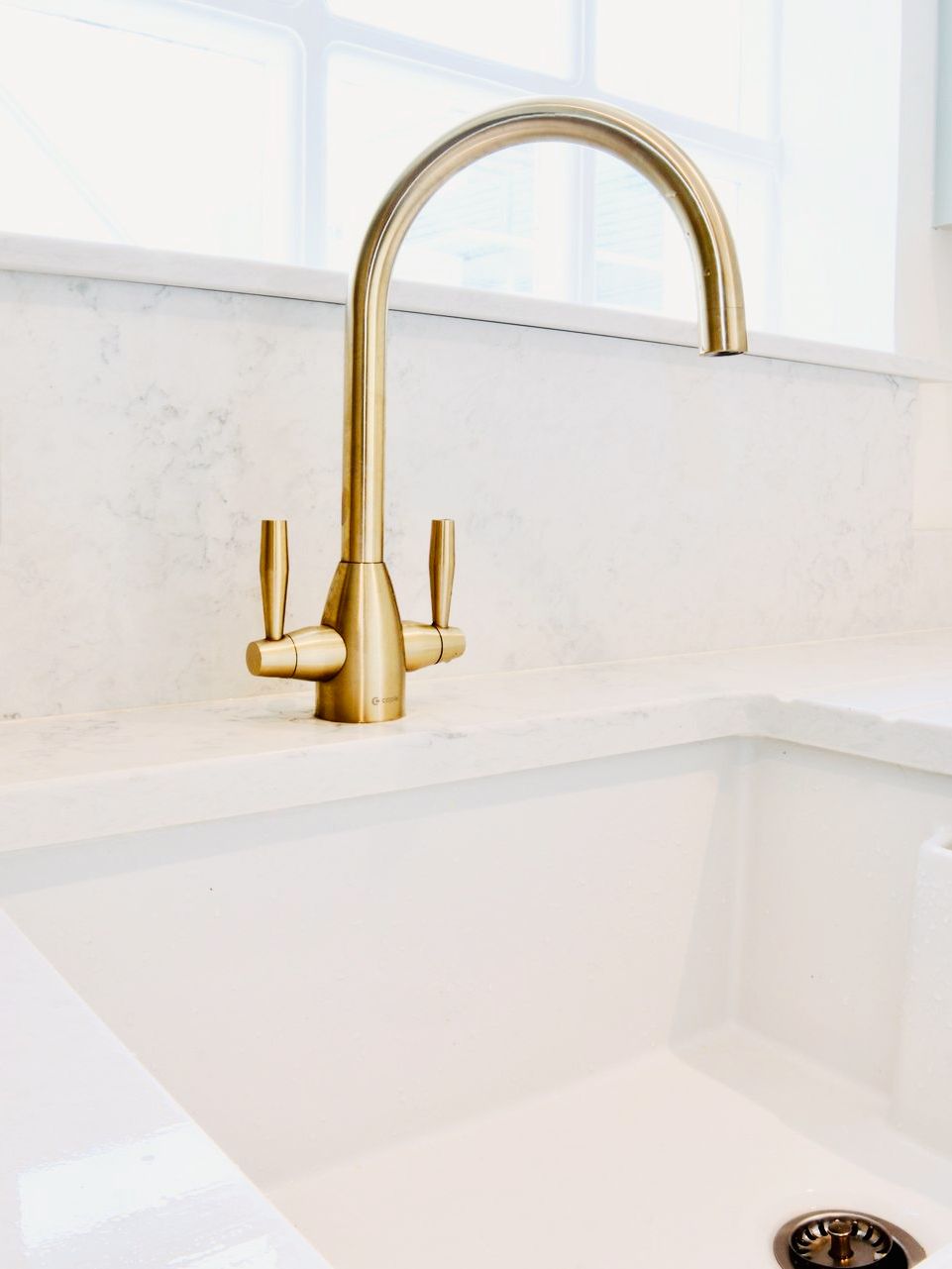 A close up of a gold faucet on a white kitchen sink.