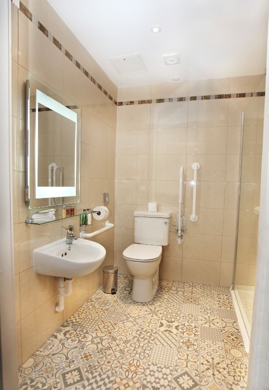 A bathroom with a toilet , sink , mirror and walk in shower.