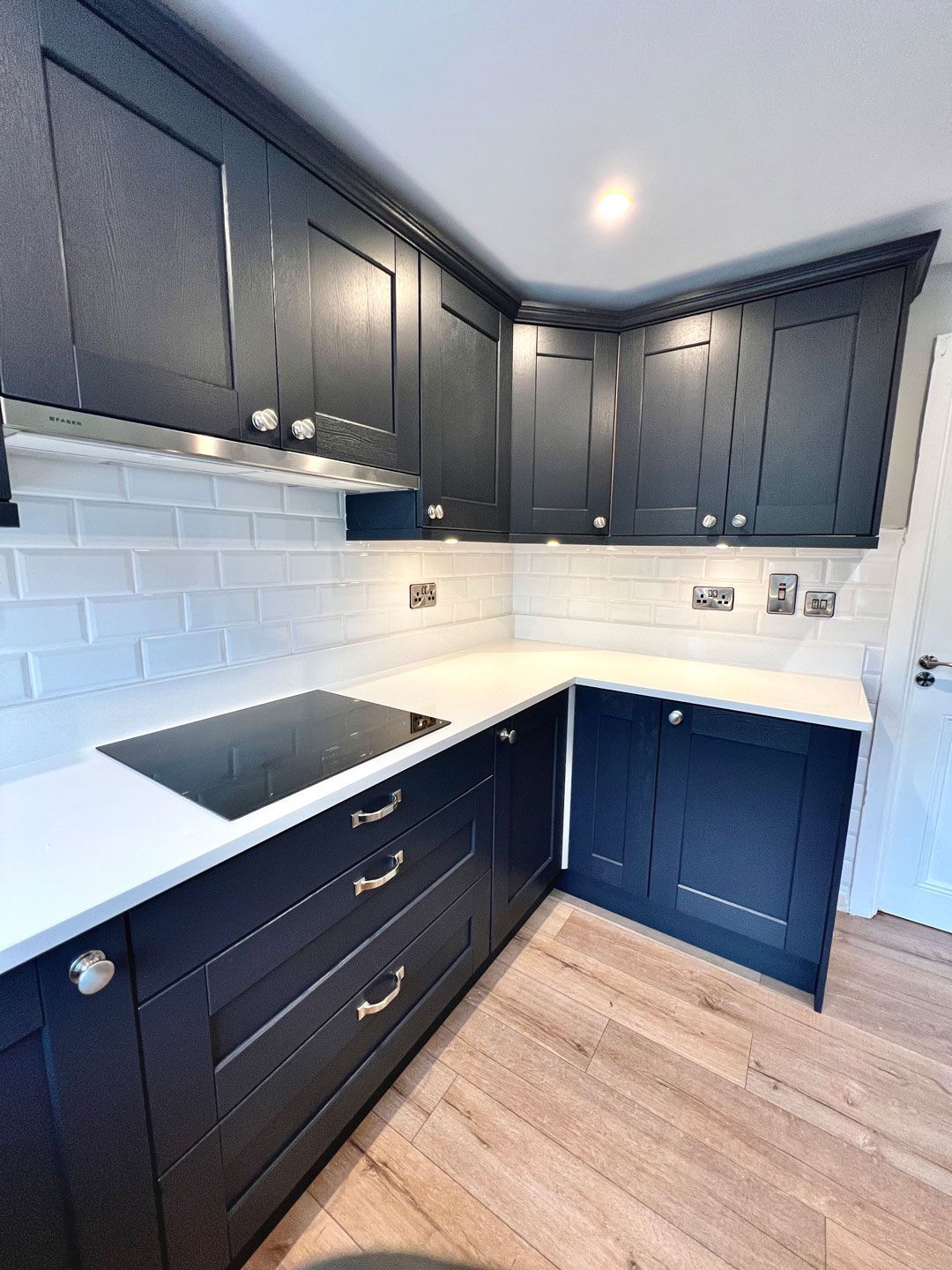 A kitchen with black cabinets , white counter tops , and a stove top oven.