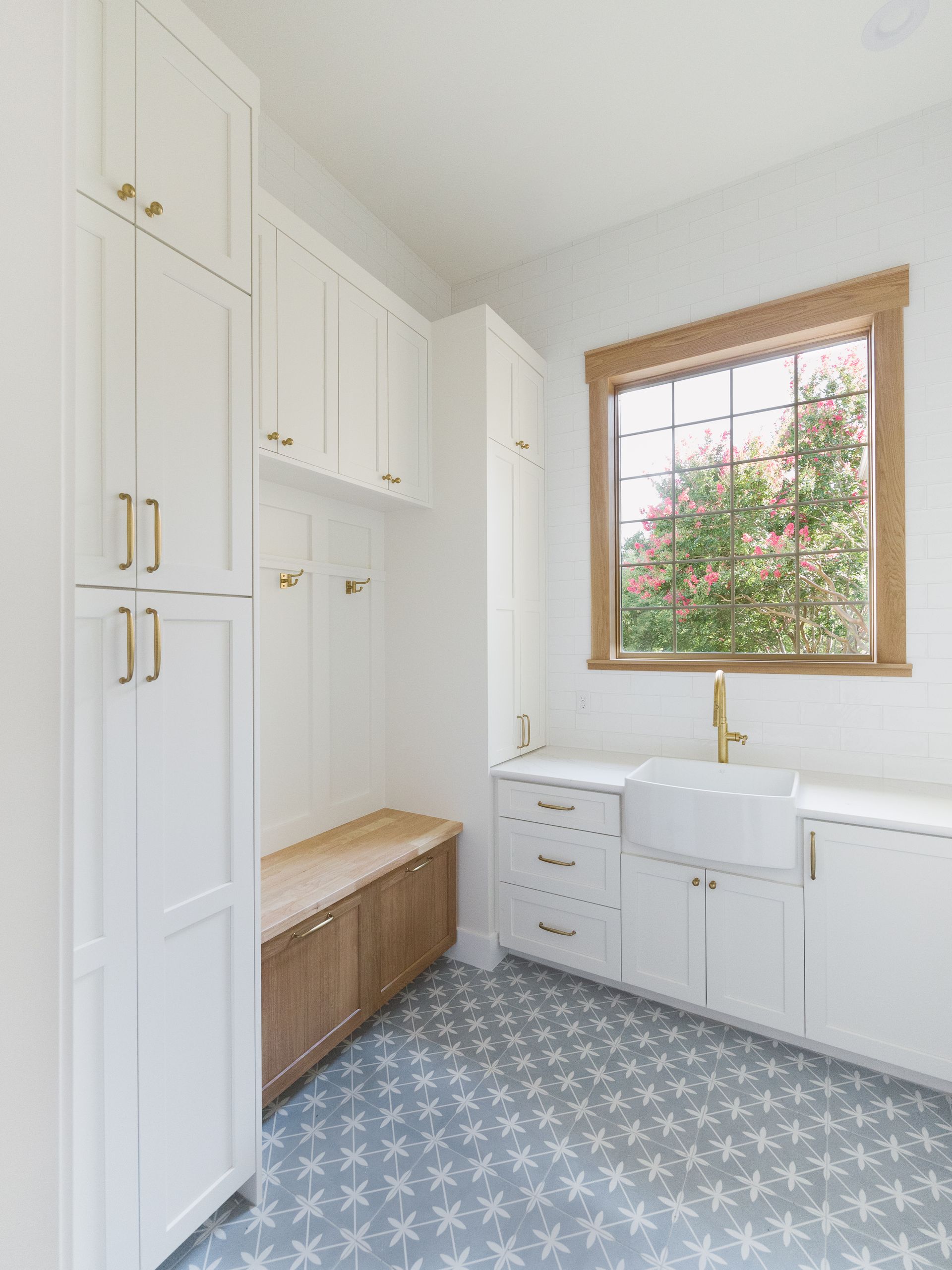 Laundry room with white cabinets, wooden bench, and patterned blue floor.