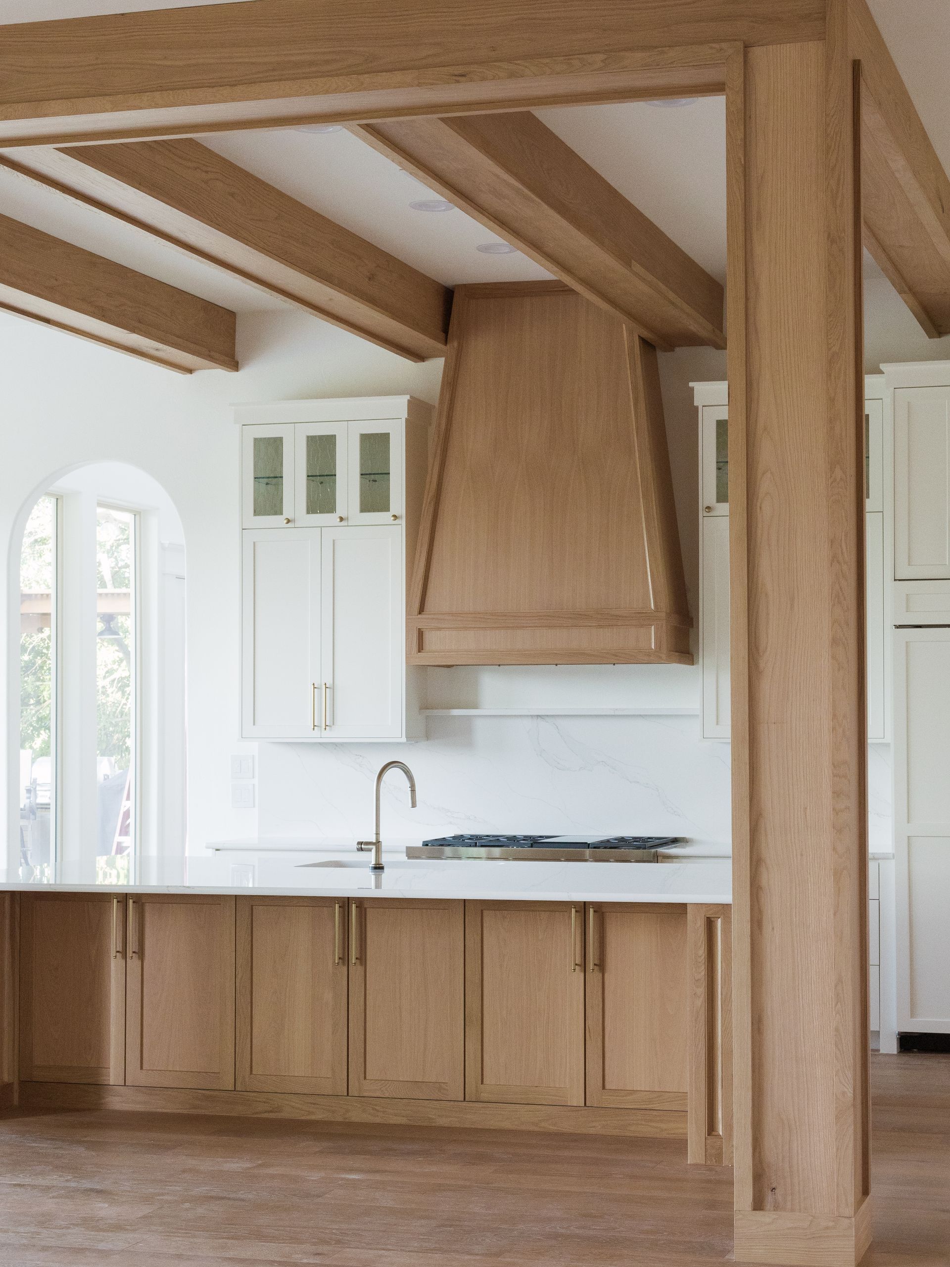 Kitchen with light wood beams, white cabinets, marble countertops, and a matching range hood.