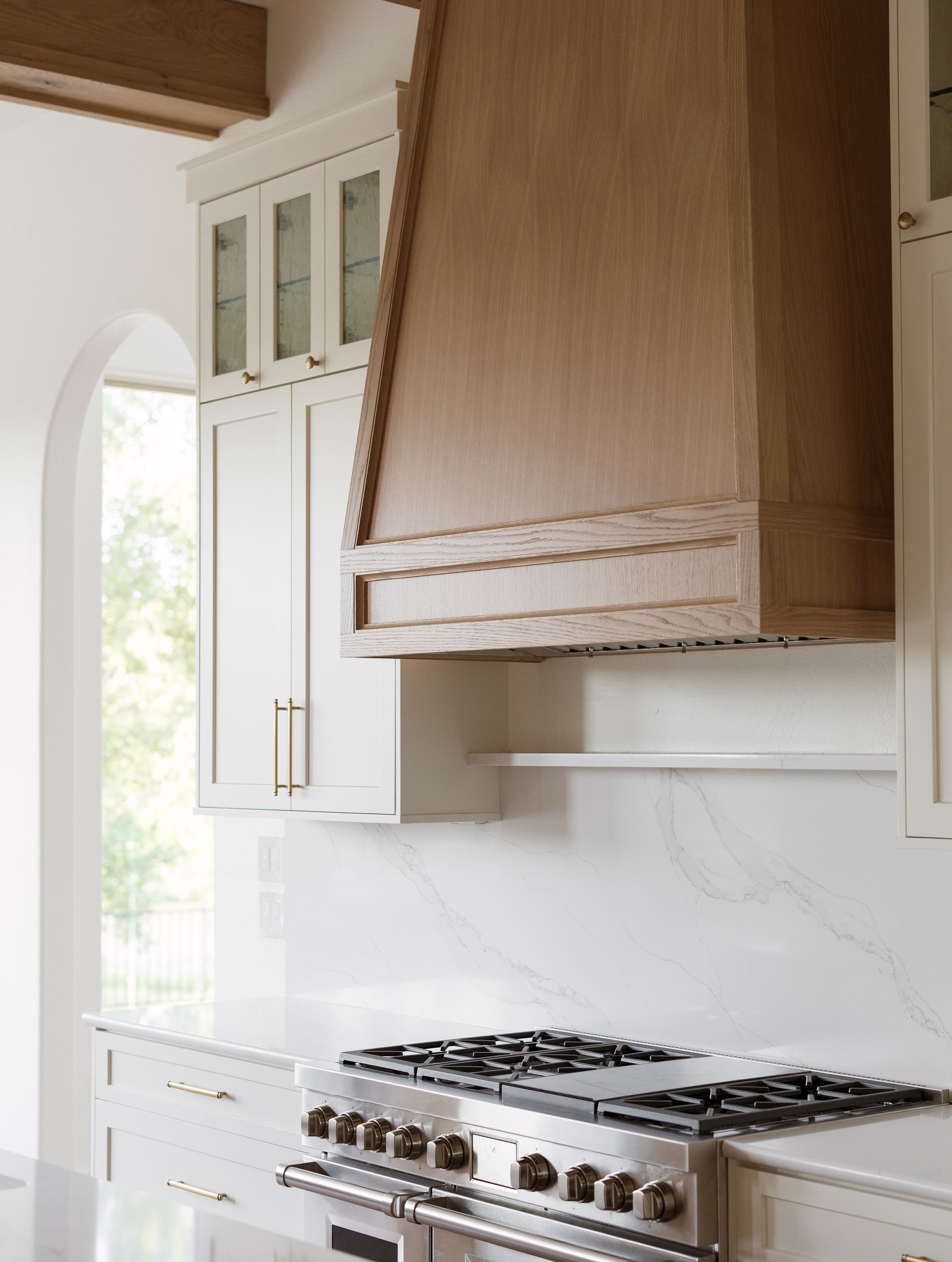 Kitchen with stainless steel range, light wood range hood, white cabinets and countertops.