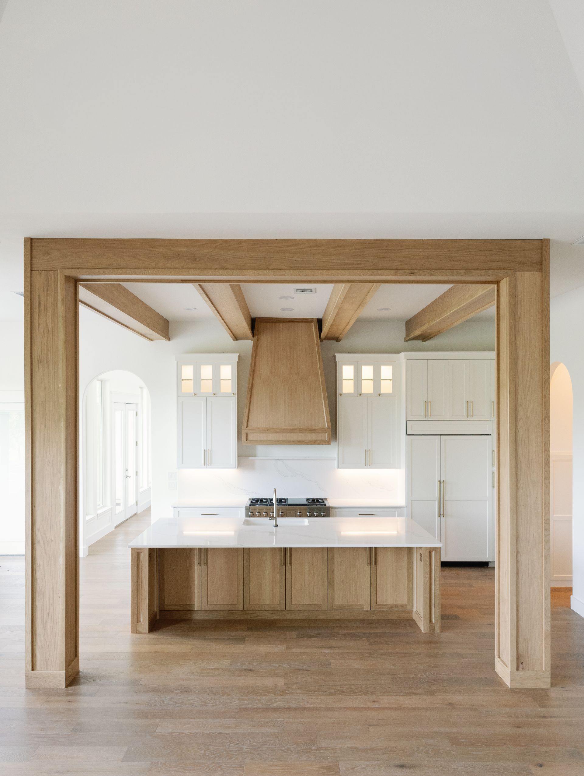 Kitchen with light wood beams, white cabinets, marble countertops, and a central island.