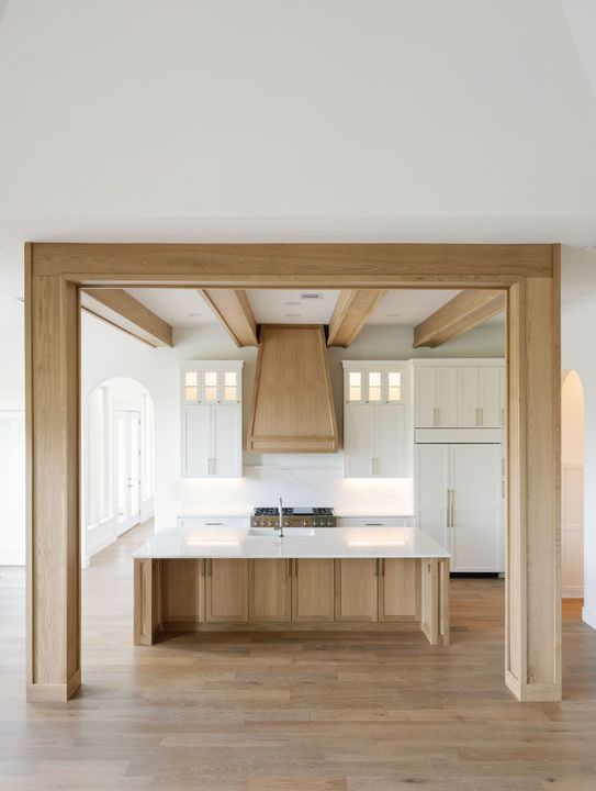 Kitchen with light wood beams, white cabinets, marble countertops, and a central island.
