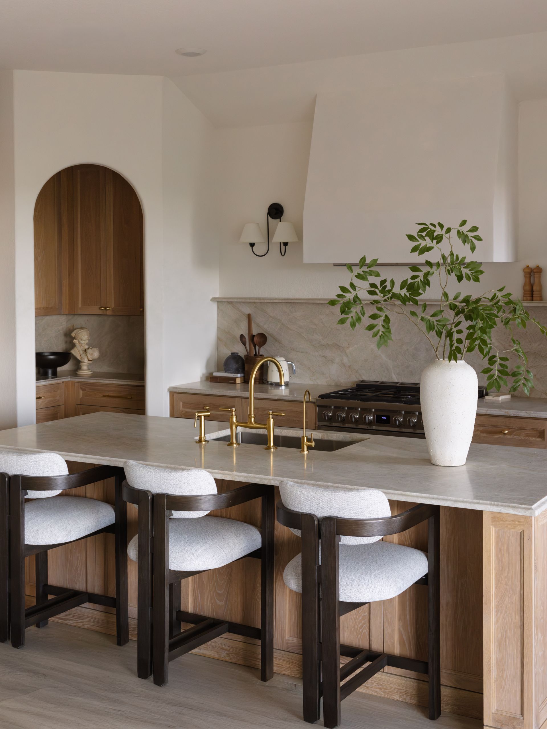 Kitchen with island and bar stools, gold faucet, white range hood, and wood cabinets.