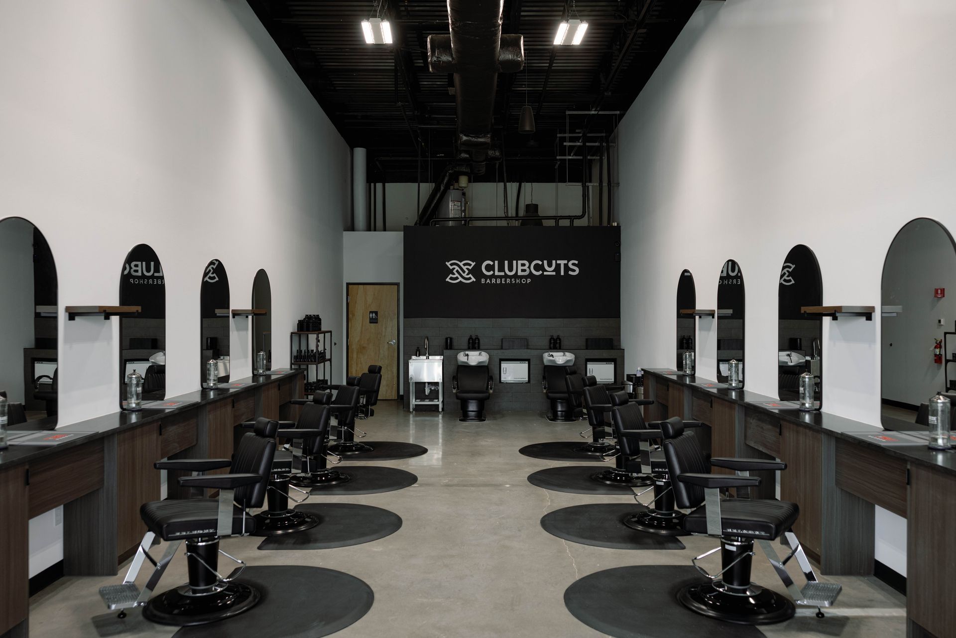 Interior of a barbershop with chairs, mirrors, and dark wood stations.  The brand logo is on the back wall.
