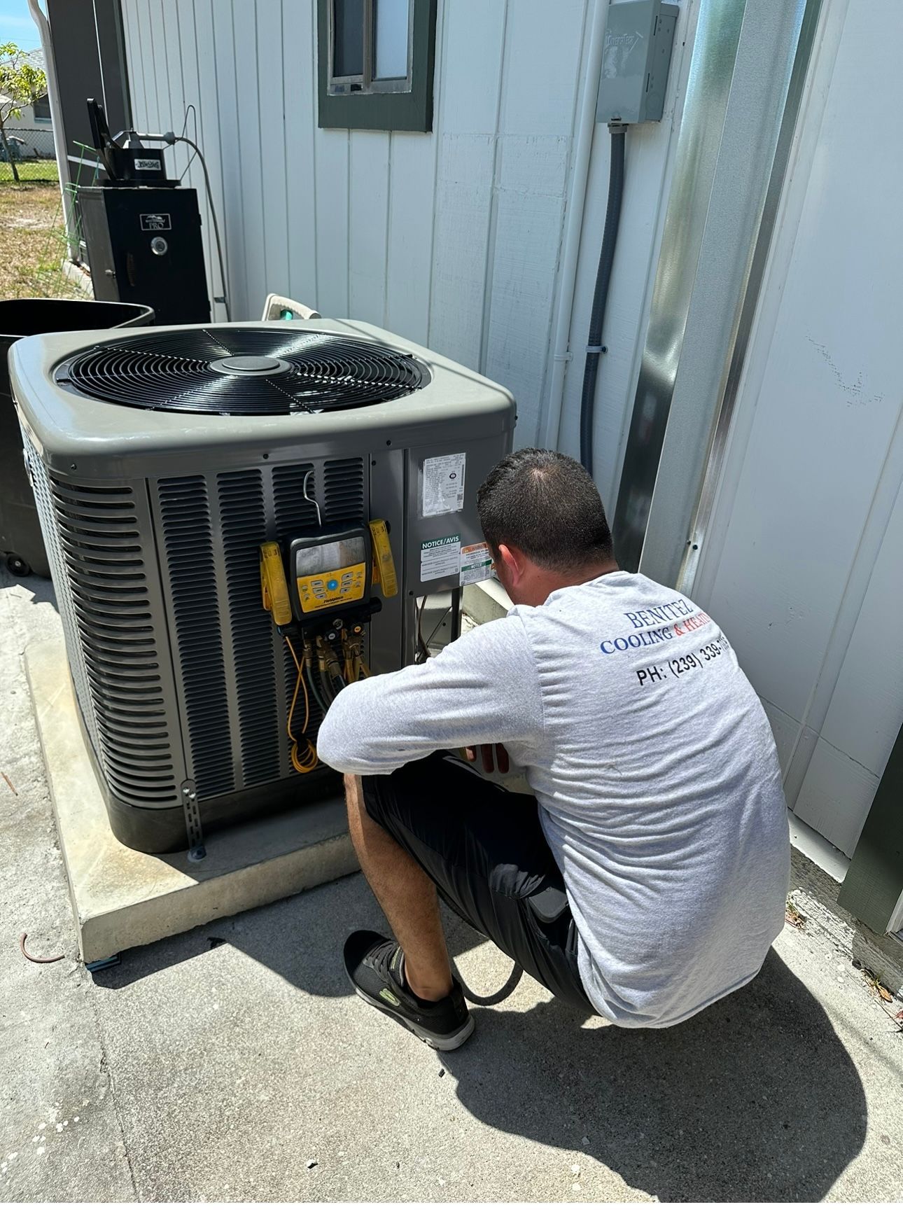 A man is kneeling down in front of an air conditioner.