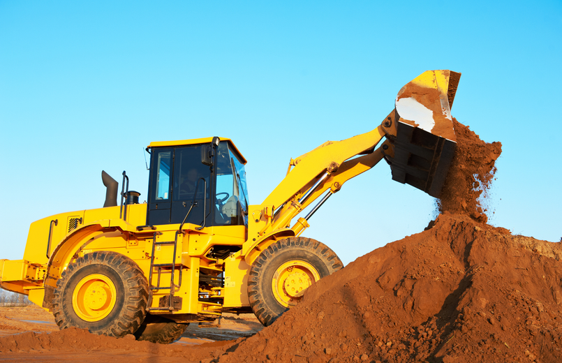 A yellow bulldozer is loading dirt into a pile.