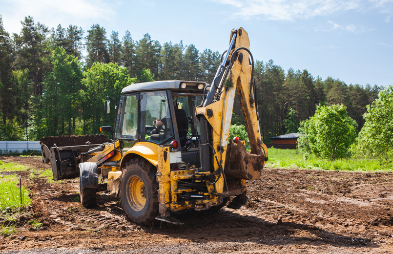 A yellow excavator is sitting in the middle of a dirt field.