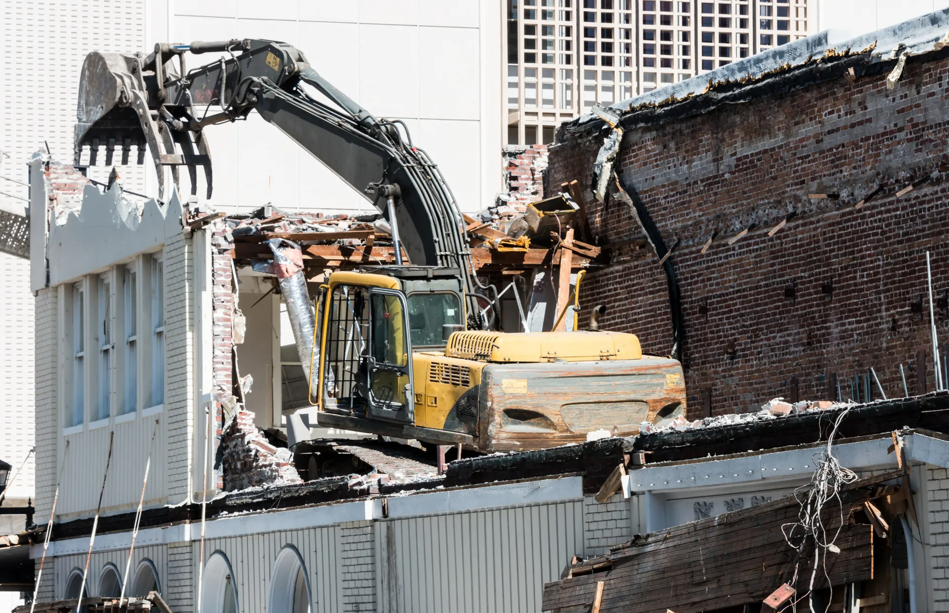 A yellow excavator is demolishing a brick building.