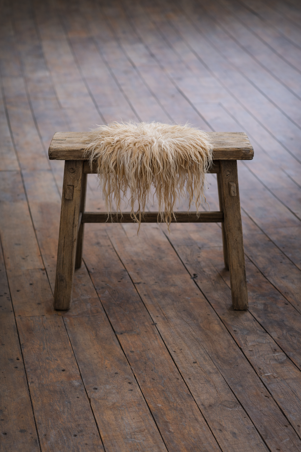 Felted fleece rug draped over a simple wooden stool and showing the natural wool texture