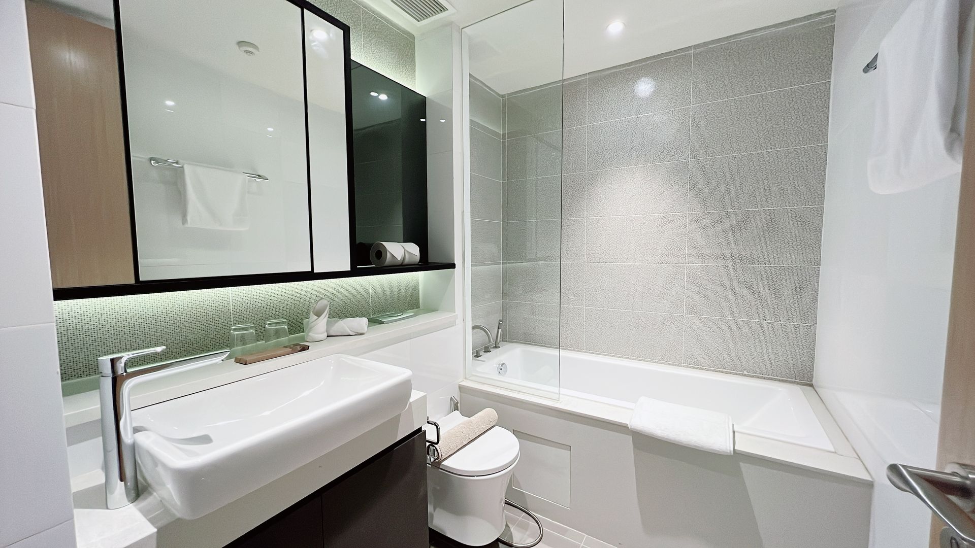 Bright modern bathroom with white tub, sink, toilet, and large mirror under soft lighting