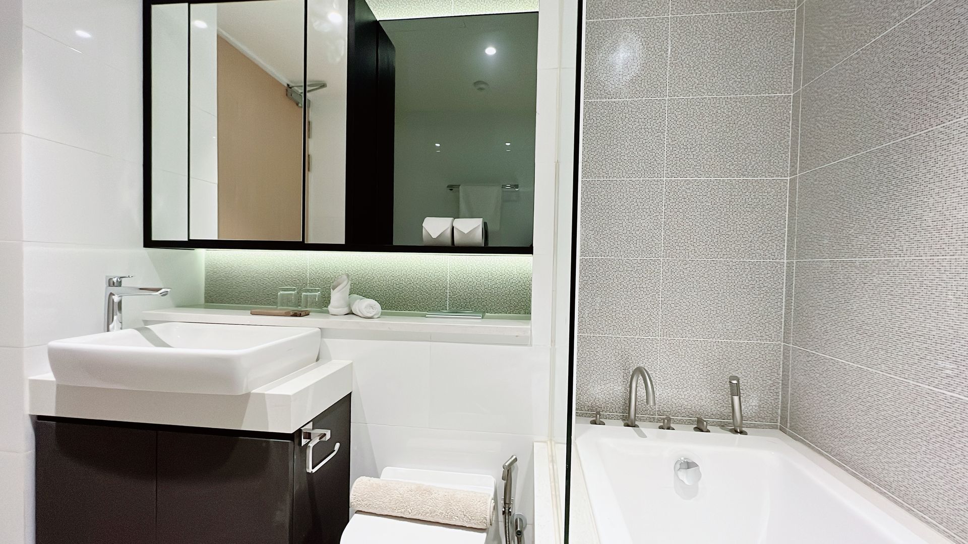 Modern white bathroom with wall mirror, sink vanity, and bathtub with patterned tile wall