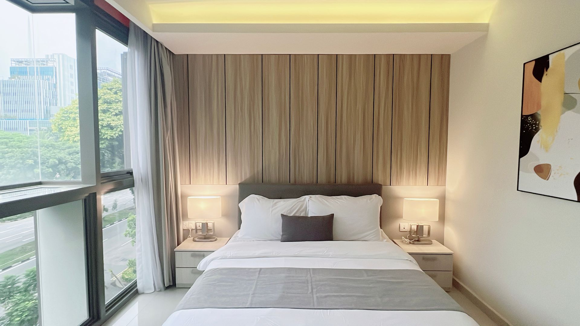 Bright modern bedroom with a made bed, floor-to-ceiling window, bedside lamps, and wood accent wall