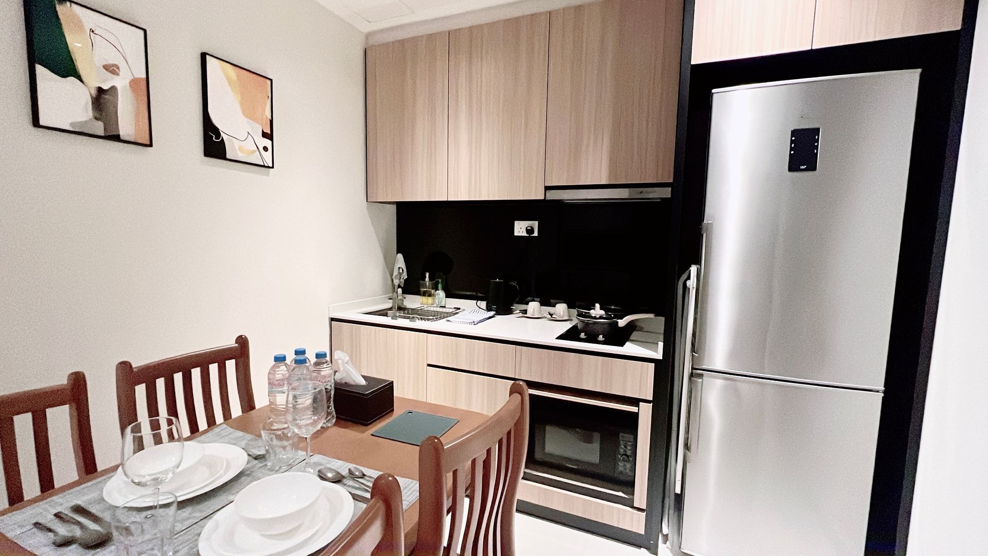 Small dining area beside a compact kitchen with wood cabinets, a refrigerator, and a set table with plates and water bottles.
