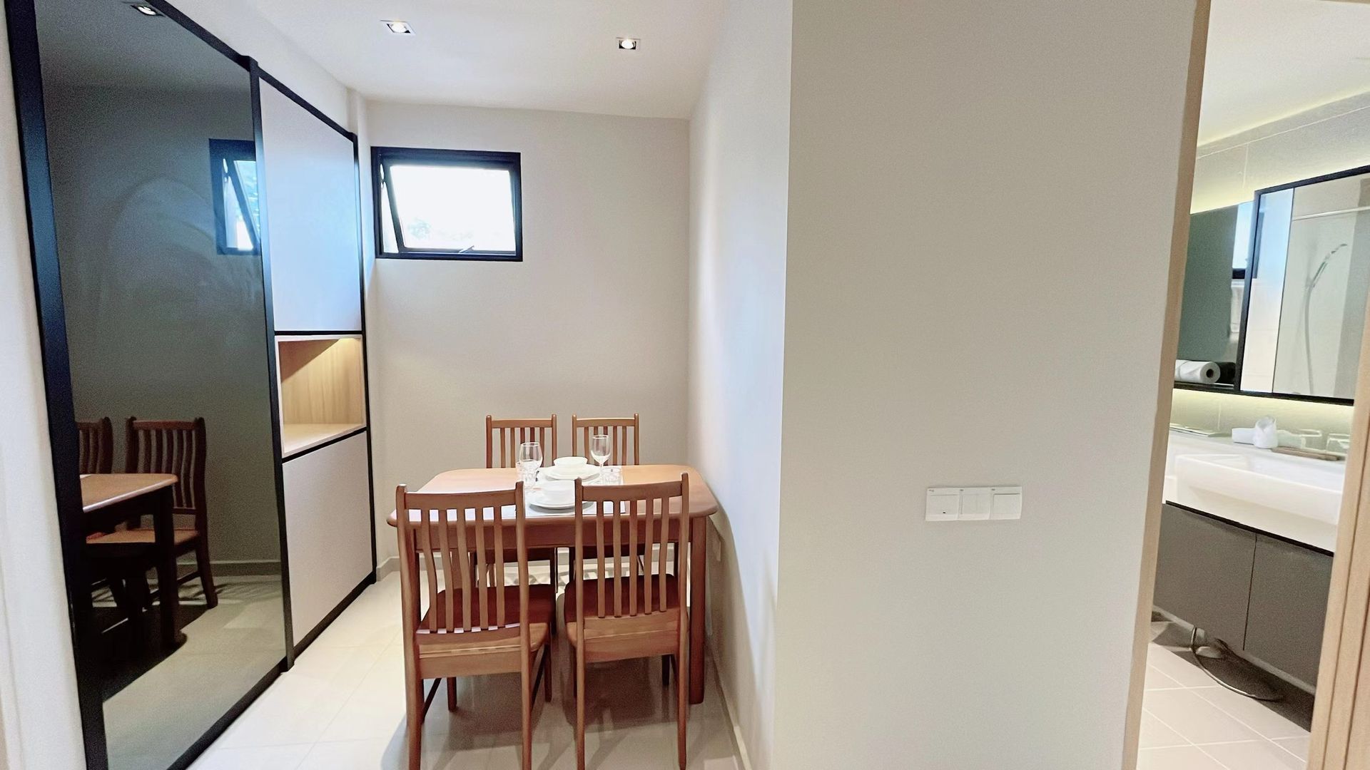 Small dining area with wooden table and chairs beside a kitchen, viewed from a hallway