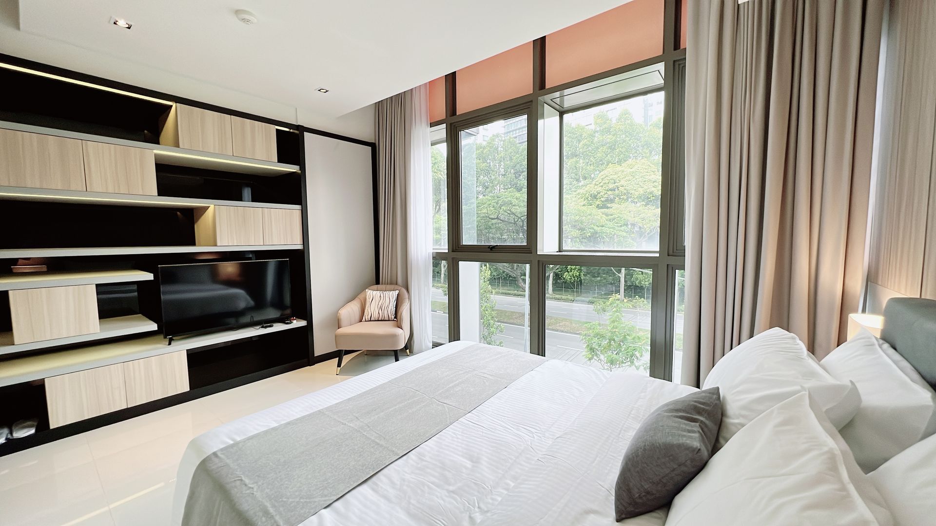 Bright bedroom with a large bed, black shelving, and floor-to-ceiling windows overlooking greenery