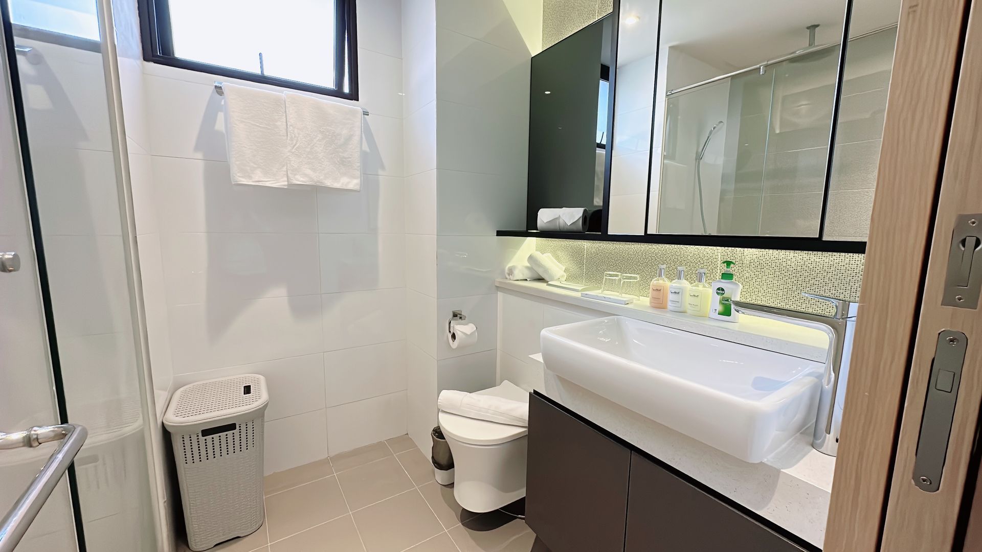Bright modern bathroom with a sink, toilet, mirror cabinet, window, and towel rack.
