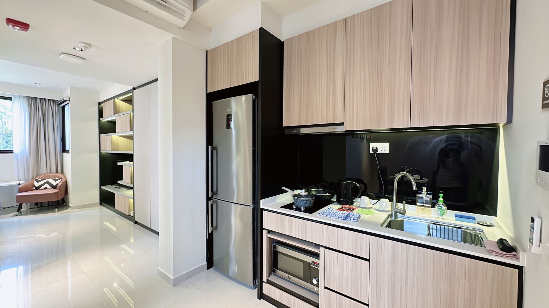 Bright modern kitchen with wood cabinets, black backsplash, and glossy white hallway leading to a bedroom