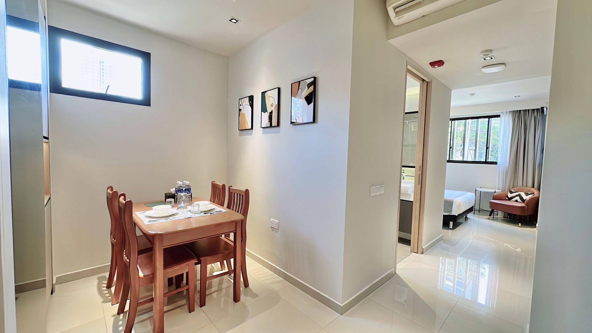 Bright modern dining area with wooden table, hallway, and a bedroom visible in the background
