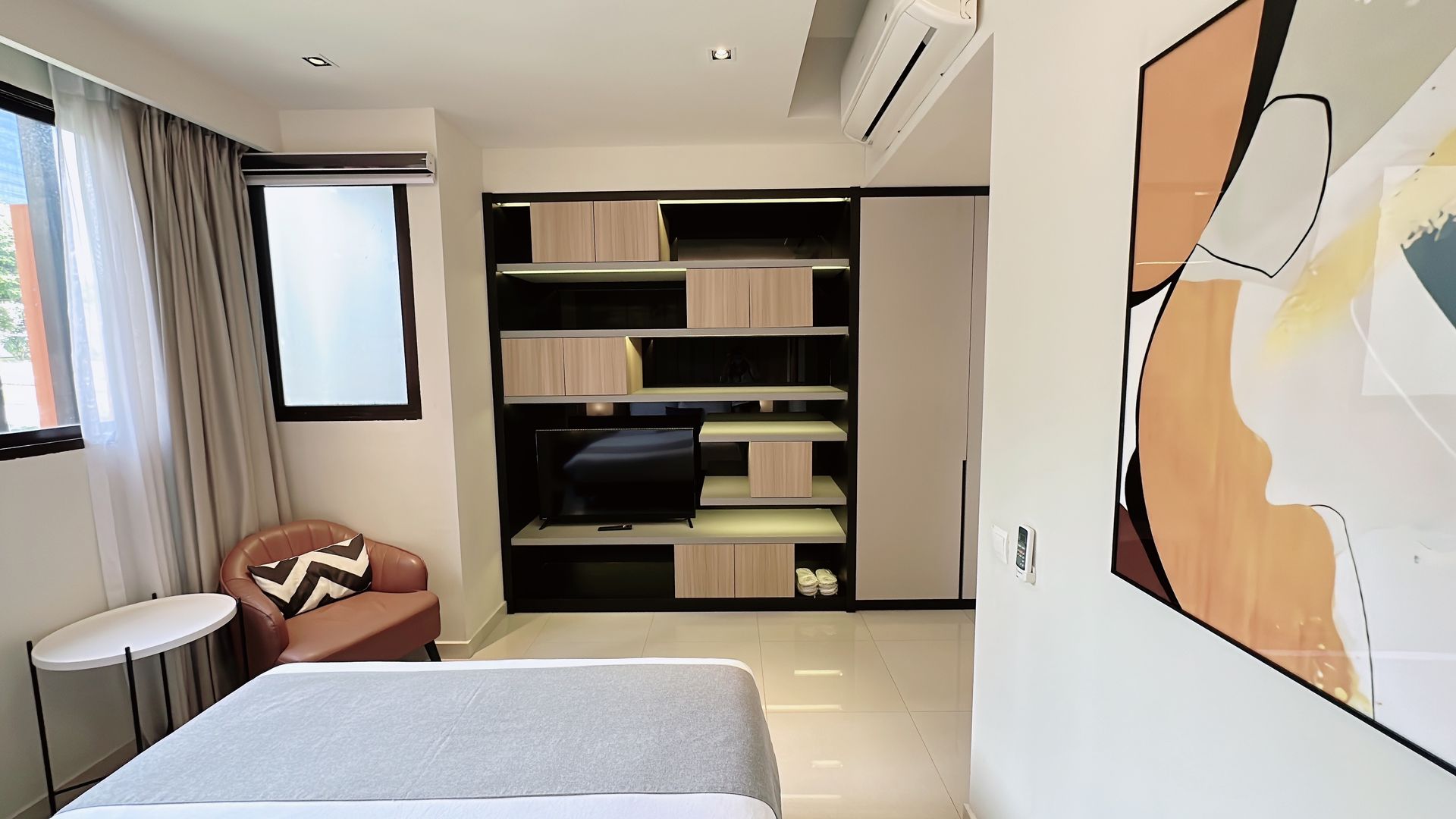 Modern bedroom with bed, built-in shelving, chair by window, and abstract wall art