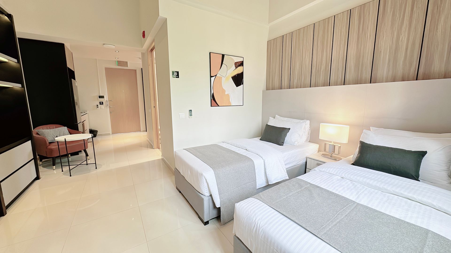 Bright hotel room with two single beds, bedside lamps, and a large mirror on the left.