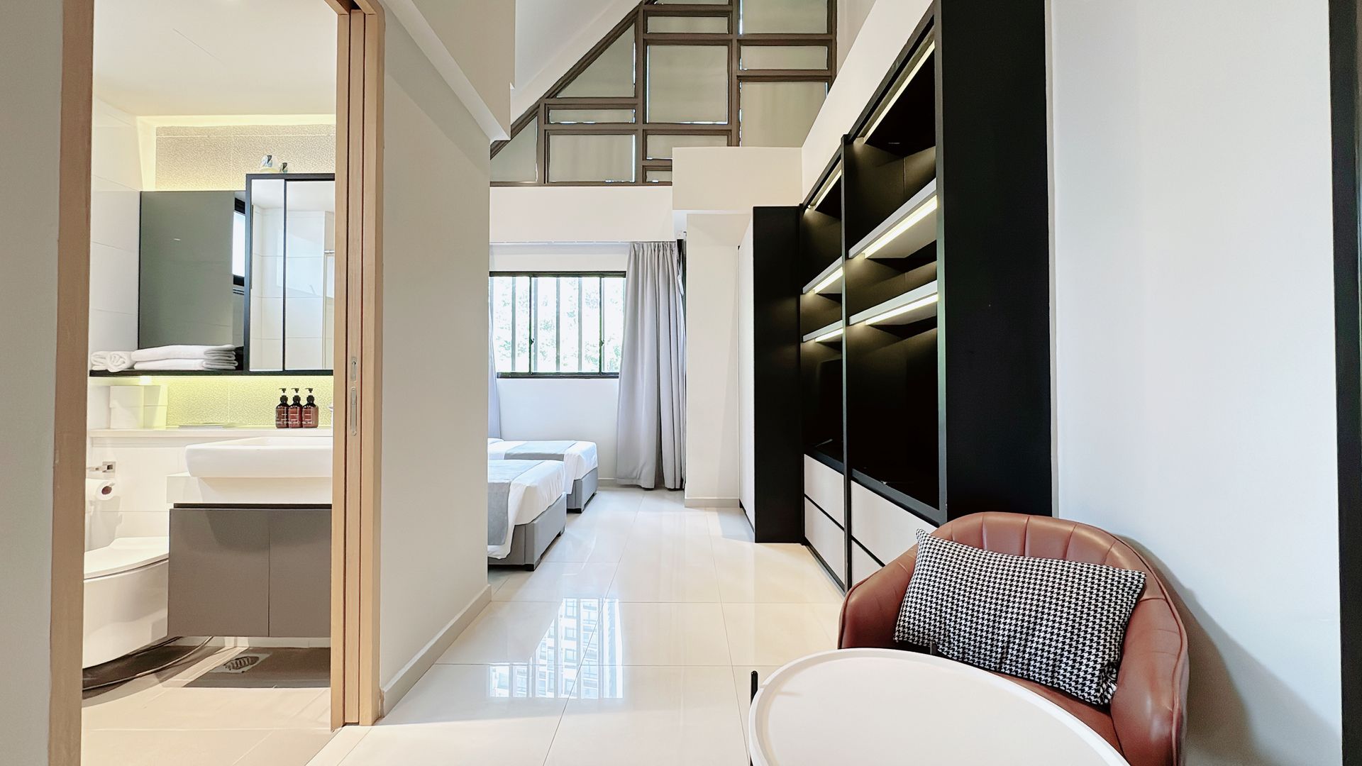 Bright modern bedroom with loft bed, built-in shelving, and an adjoining bathroom visible through a doorway