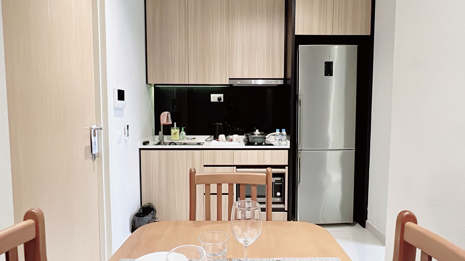 Small dining area with a table and chairs facing a compact kitchen and refrigerator.