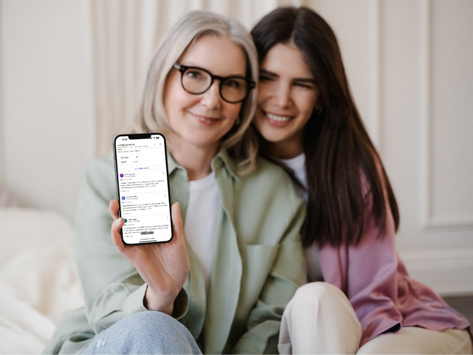 Deux femmes sont assises sur un canapé et tiennent un téléphone portable.