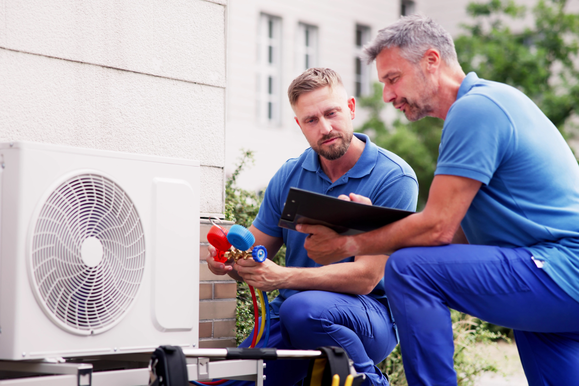 Deux hommes travaillent sur un climatiseur à l'extérieur d'un bâtiment.