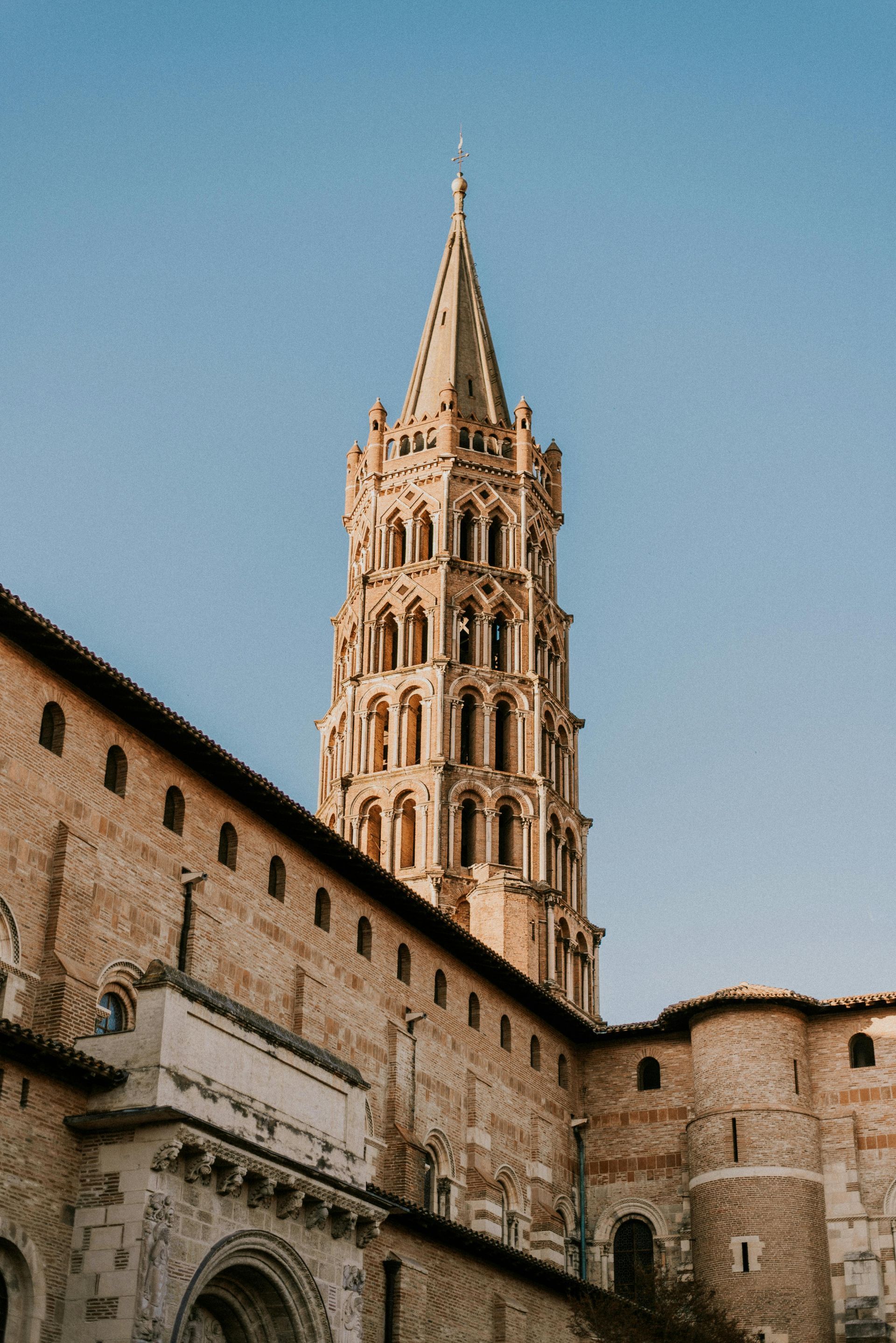 Église en pierre avec un haut clocher contre un ciel bleu clair.