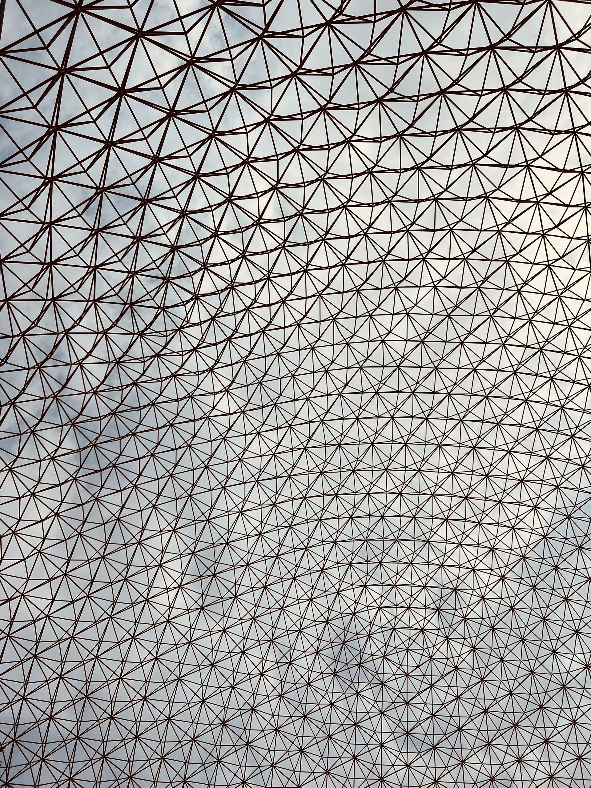 Geometric metal lattice against a cloudy sky, forming a complex structure.