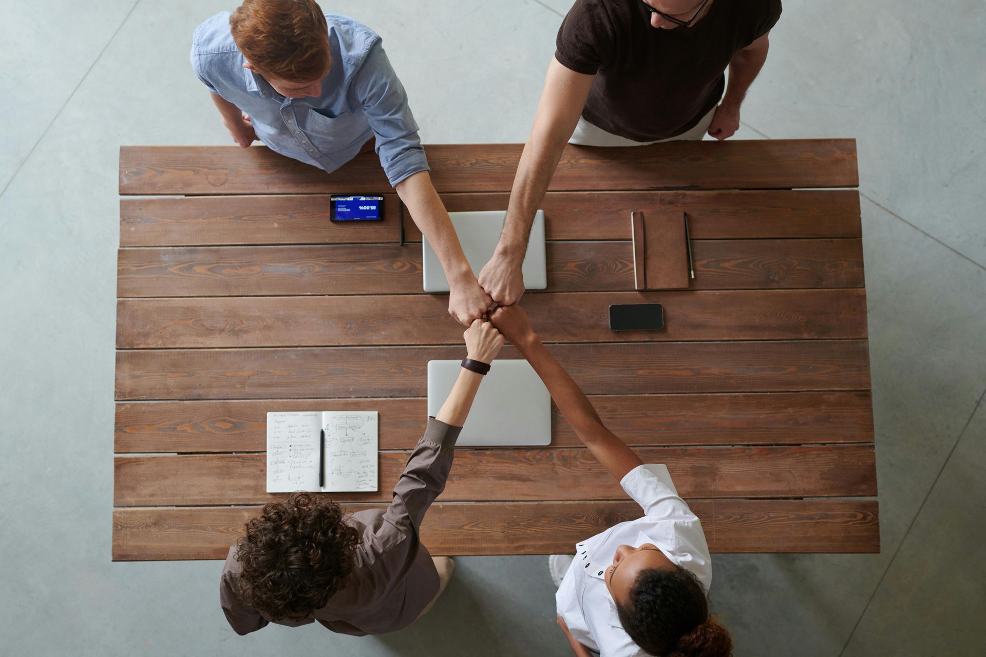 Un groupe de personnes sont assises à une table en bois et mettent leurs mains ensemble.