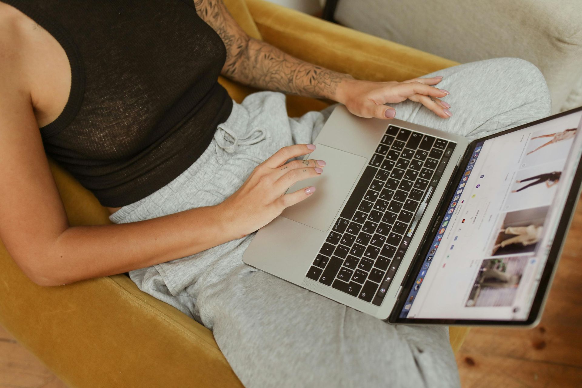 Person in black tank top and sweatpants using a laptop, sitting in a yellow armchair.
