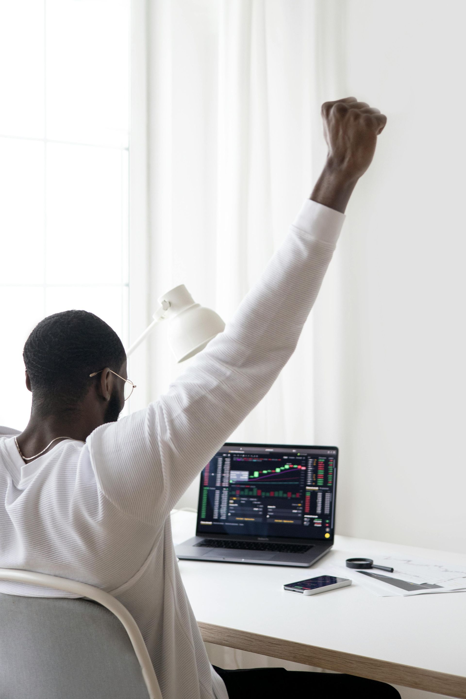 Man celebrates with fist raised in front of laptop showing financial charts.